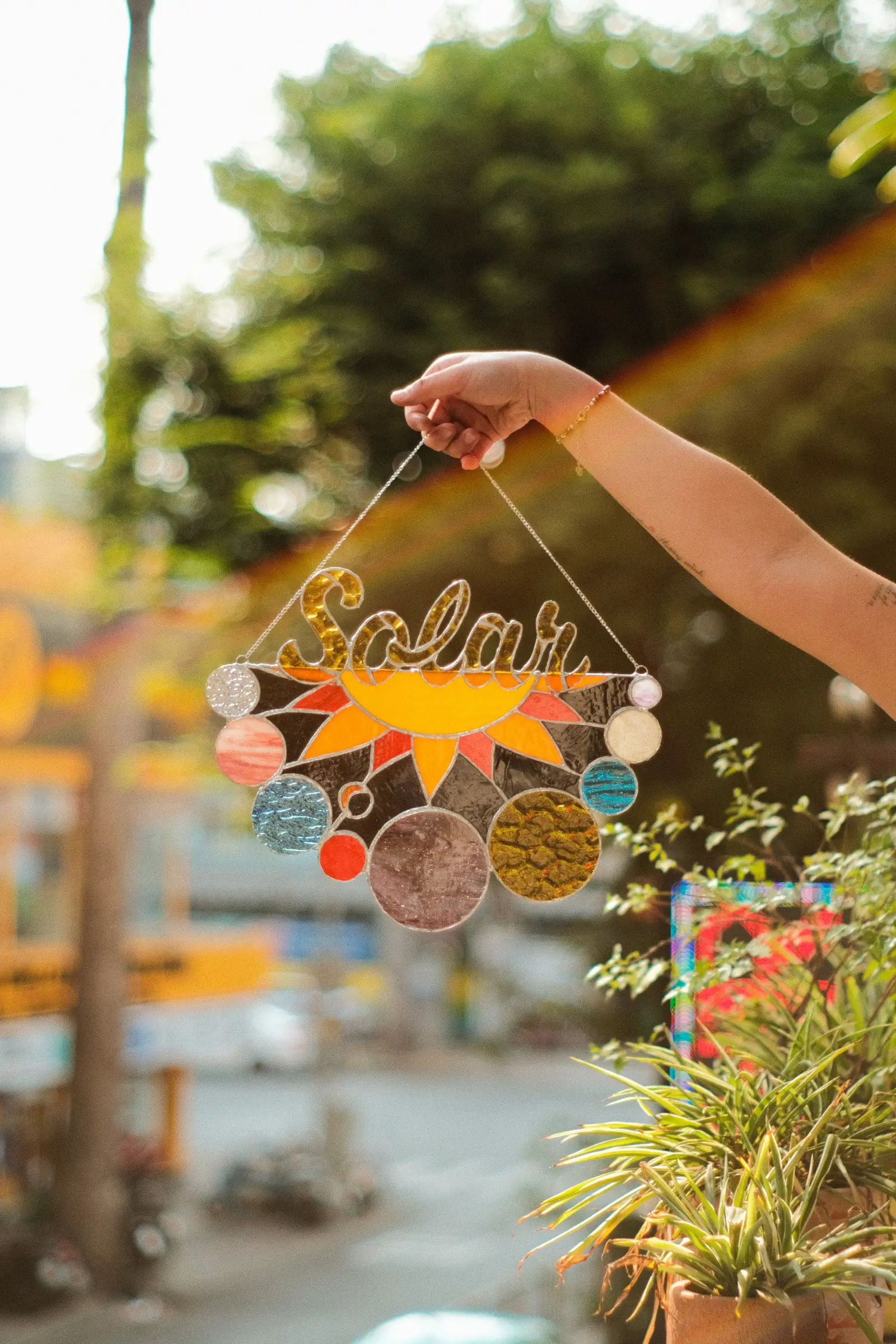 Bàn tay giơ một tấm suncatcher kính màu lên ngược sáng ngoài trời